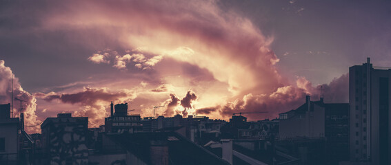 A panoramic shot of a dramatic sunset in Lisbon with silhouettes of residential and office houses; the panorama of stunning evening cloudscape over the cityscape with purple colour tint