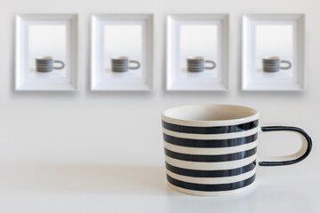 Mug in black and white stripes, on a white table. On the wall are photographs of this mug in four frames. Vertical frame. Space for text.