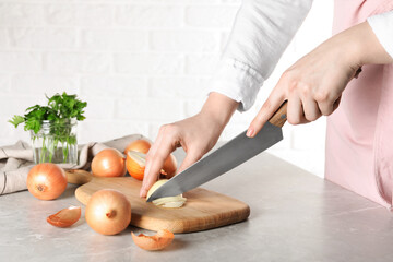 Woman cutting ripe onion at grey textured table, closeup