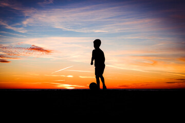 silhouette of boy playing soccer at sunset on beach