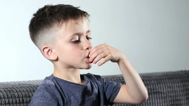 A little boy opening sweets and taking pastila his mouth while sitting on a cozy sofa. A child enjoys candy