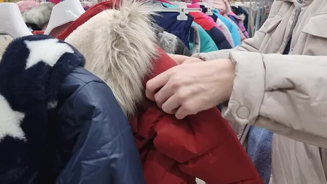 a woman chooses and examines coats and jackets in a store or second-hand store.
