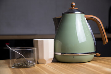 stylish teapot, cup and green tea with teaspoon stand on wooden table in kitchen