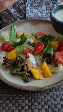 M&atilde;os colocando molho na salada de r&uacute;cula, alface, tomate cereja e manga.