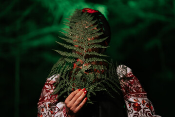 Portrait of ukrainian woman with fern at night in Carpathian mountains forest.