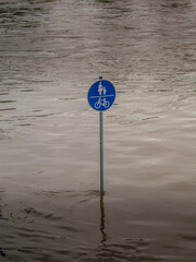 Foot and bike path flooded during a flood. Only a traffic sign still indicates this.
