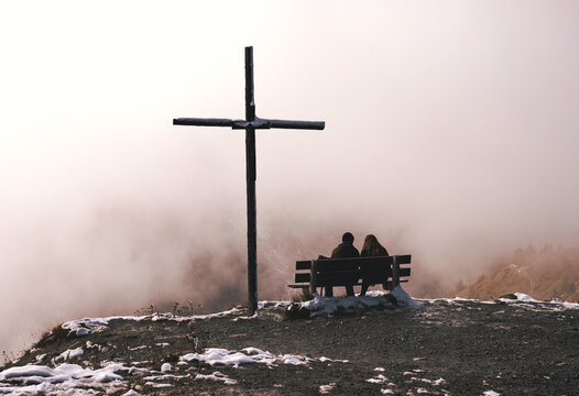 people sitting on a bench near a cross