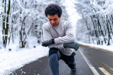 Young man resting and stretching after running in mountain road on cold winter day.