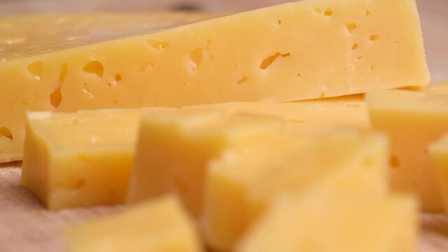 Camera moves along slice of yellow cheese with holes on cutting board. 