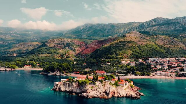Areal shot over the picturesque little village-Sveti Stefan.Houses and buildings surrounded by the sea.4K drone shot of the beach and favourite tourist destination.Beautiful landscape.Blue clear sea.