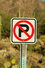 No parking sign with red and black paint on white background with metal pole holding it up in late afternoon sun