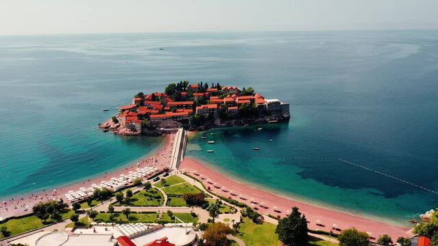 Areal shot over the picturesque little village-Sveti Stefan.Houses and buildings surrounded by the sea.4K drone shot of the beach and favourite tourist destination.Beautiful blue clear water.