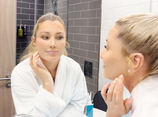 woman looking in the mirror in the bathroom and taking care of her skin.