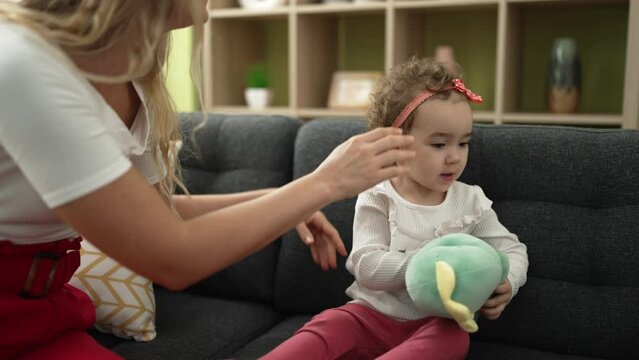 Woman and toddler combing hair with hands sitting on sofa at home