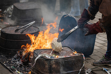 Baked ceramic bowl held by tongs with protective gloves being loaded into a reduction fire made...