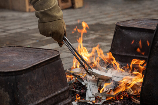 Western Raku reduction bins being loaded with ceramic pottery using heat resistant gloves and tongs into a fire made with newspaper strips