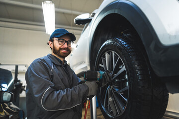 Fototapeta na wymiar Low-angle shot of a smiling mechnic screwing a car wheel. Repair shop concept. High quality photo