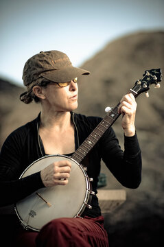 A woman practices the banjo outdoors.