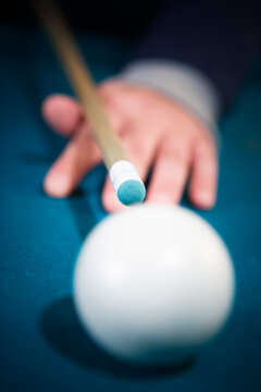 Cue stick and hand from behind a white que ball.