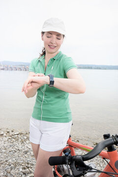 Mature woman with electric bike by lake checking the time, Bavaria, Germany