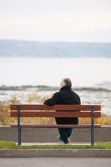 Rear view of mature man overlooking river in Autumn alone.