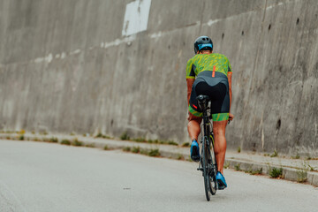 Full length portrait of an active triathlete in sportswear and with a protective helmet riding a bicycle. Selective focus 