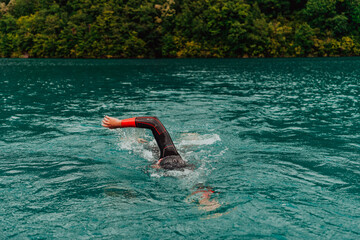 A triathlete in a professional swimming suit trains on the river while preparing for Olympic swimming