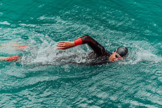 A triathlete in a professional swimming suit trains on the river while preparing for Olympic swimming - Powered by Adobe