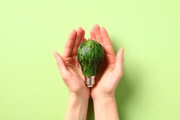 Eco-friendly light bulb with green leaves in woman's hands. Saving energy, protecting the environment and conserving resource concept
