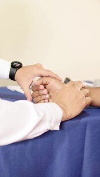 doctor looking at his watch while palpating radial and ulnar pulse on wrist of unrecognizable woman