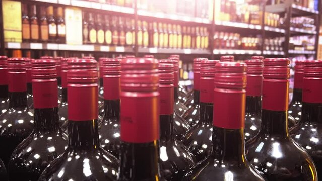 Rows of red wine bottles stand in a warehouse of a liquor store or supermarket