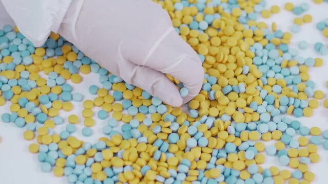 hands in latex gloves sort through multi-colored pills from palm to palm on a bedlam background