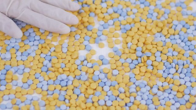 hands in latex gloves sort through multi-colored pills from palm to palm on a bedlam background Close up