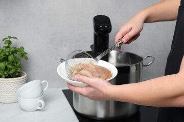 Woman taking out vacuum packed meat from pot in kitchen, closeup. Thermal immersion circulator for sous vide cooking