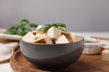 Bowl of smoked tofu cubes and basil on wooden tray, closeup