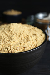 Bowl of aromatic mustard powder on black wooden table, closeup