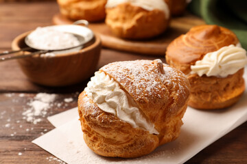 Delicious profiteroles with cream filling and powdered sugar on wooden table, closeup