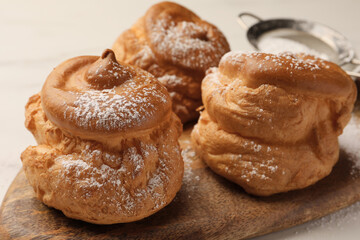 Delicious profiteroles with powdered sugar on wooden board, closeup