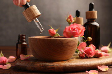 Fototapeta na wymiar Woman dripping essential oil into bowl at wooden table, closeup. Aromatherapy treatment