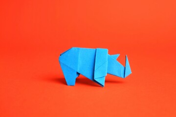 Origami art. Handmade light blue paper rhinoceros on orange background