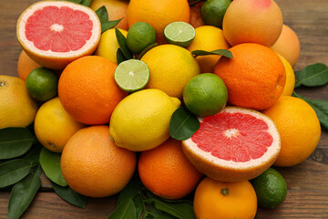 Different citrus fruits with green leaves on wooden table, closeup