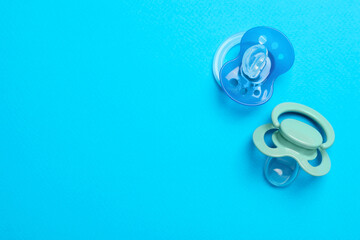 Flat lay composition with pacifiers and other baby stuff on light blue background. Space for text