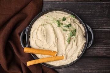 Delicious hummus with grissini sticks on wooden table, top view
