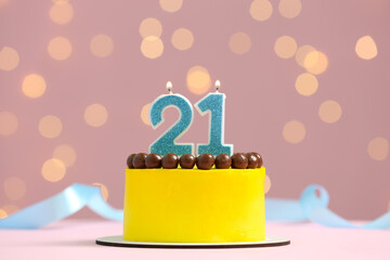 Coming of age party - 21st birthday. Delicious cake with number shaped candles on pink background against blurred lights