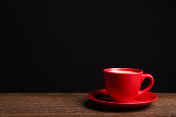 Red ceramic cup with hot aromatic coffee on wooden table against black background, space for text