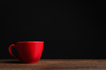 Red cup on wooden table against black background, space for text
