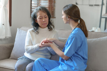 Obraz premium Portrait of attractive young caucasian female nurse elderly caregivers with senior patient home caring for elderly asia female patients on couch, indoors. hand clasp to encourage