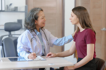 Fototapeta premium Female elder doctor takes a history of a patient and gives a consultation about osteopathy to a female patient after measuring blood pressure and heart rate and encouragement by holding hands