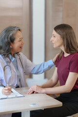 Female elder doctor takes a history of a patient and gives a consultation about osteopathy to a female patient after measuring blood pressure and heart rate and encouragement by holding hands