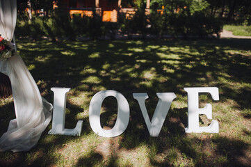 The word "LOVE" from large three-dimensional white letters on green grass. Decor for wedding romantic ceremony.